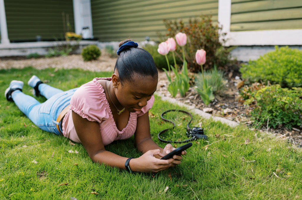 Young teenage black girl lying in grass while on her phone