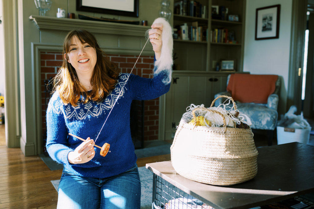 smiling woman working with her drop spindle in living room