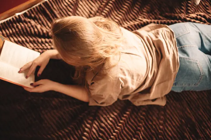 High angle view of young woman reading book lying on bed at home