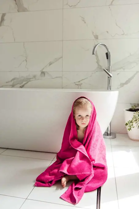 little girl sitting on the floor in the bath in a pink towel