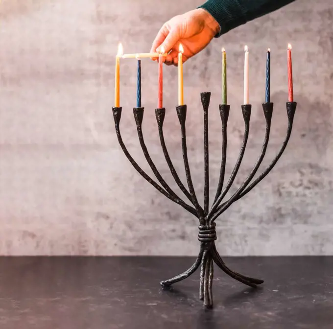 Cropped image of a hand lighting candles on menorah for Hanukkah.