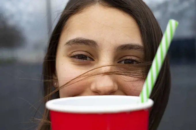 Woman with her hair on her face holding a cup with a straw.