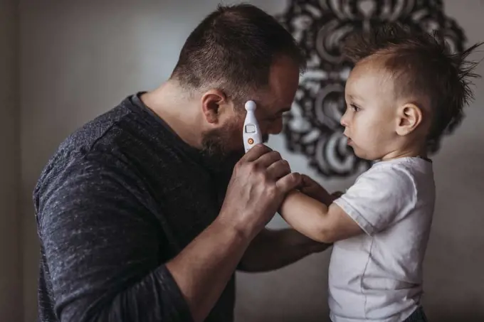 One year old boy taking fatherâ€™s temperature at home during isolation
