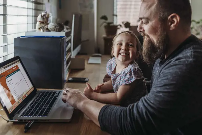 Young preschool aged daughter smiling at dad while he works from home