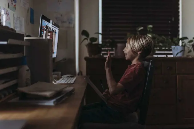 Side view of young boy waving to friends on video chat
