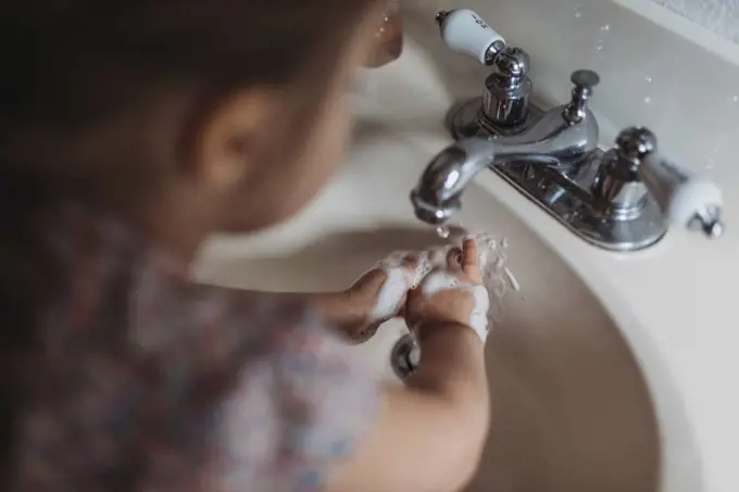 Young preschool aged girl washing hands in sink with soap
