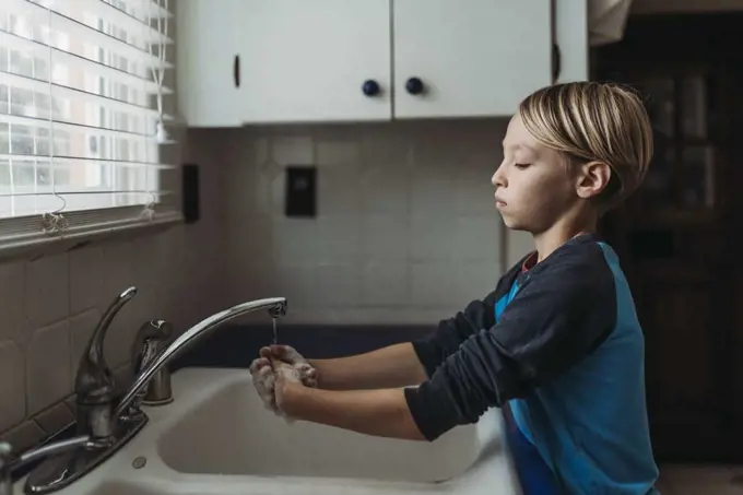 Side view of school aged boy wasking hands at sink in kitchen