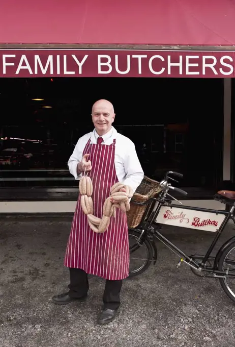 Butcher holding sausage in front of his shop