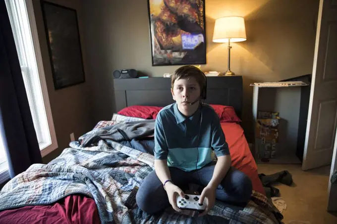 High View of Teen Boy Gaming While Wearing Headset, Sitting on Bed