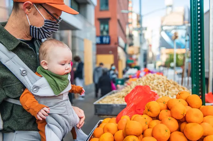 Father with cute baby girl buying persimmons on street in city during coronavirus crisis