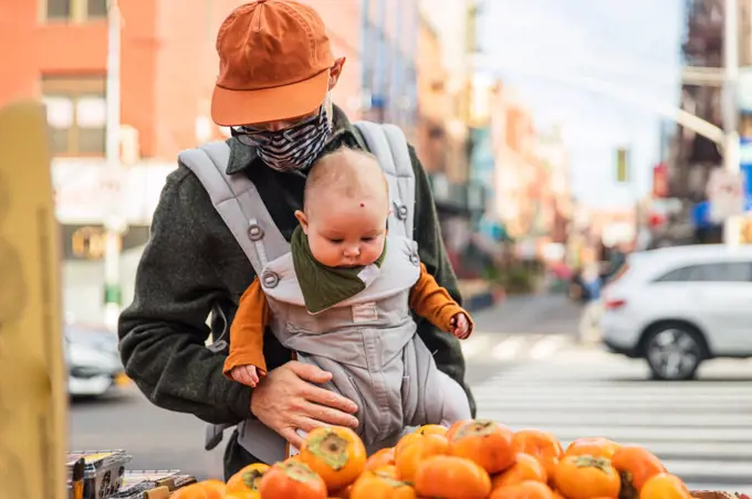 Father with baby girl buying persimmons on street in city during coronavirus outbreak