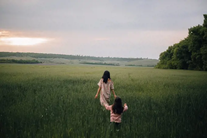 mother and daughter walking in field at sunset