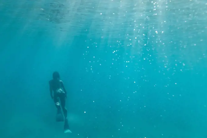 female free diver swims away in the teal waters off oahu, hawaii