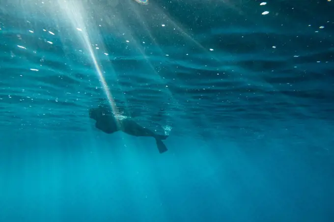 Female snorkels through light streaks at the surface of oahu ocean