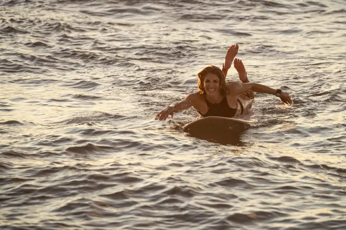 Athletic female paddles on surf board at sunset in hawaii