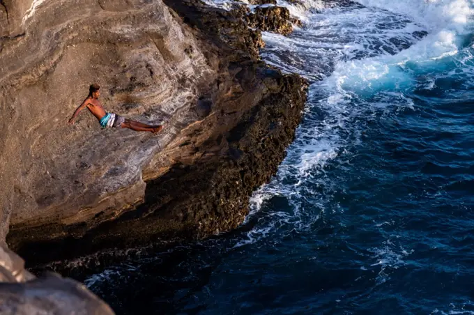 Athletic male cliff diver jumps into ocean in oahu, hawaii
