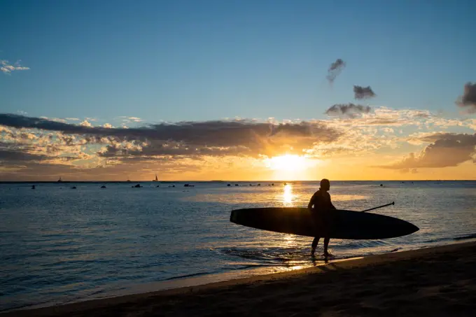 Stand up Paddler walks out of hawaii ocean at sunset