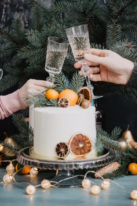 Male and female hands clink glasses near festive christmas cake on new year's eve