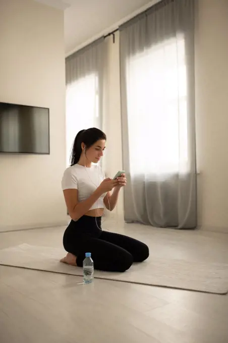 Female sitting on mat and browsing smartphone