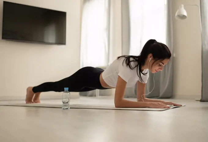 Young female planking with earphones and smartphone