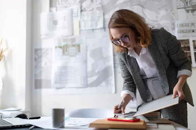 Serious businesswoman with clipboard reading notes on smartphone
