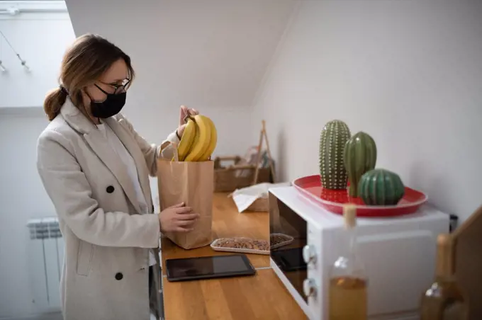 Woman in mask taking purchases from bag at home