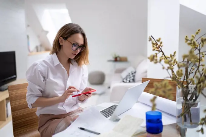 Busy woman working at home and using smartphone