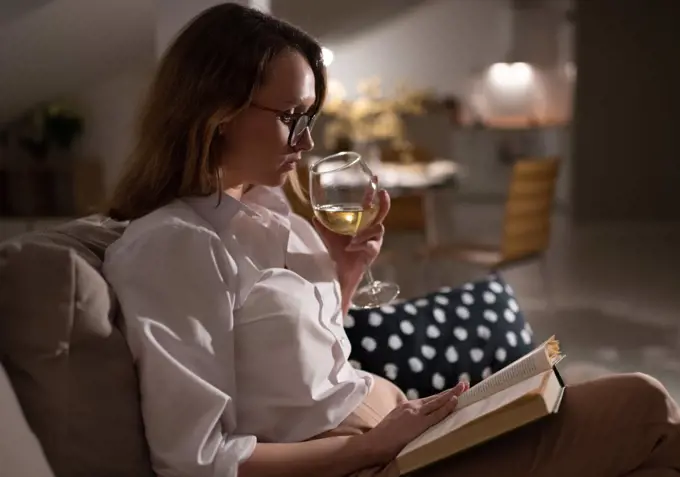 Relaxed woman enjoying wine and book at home