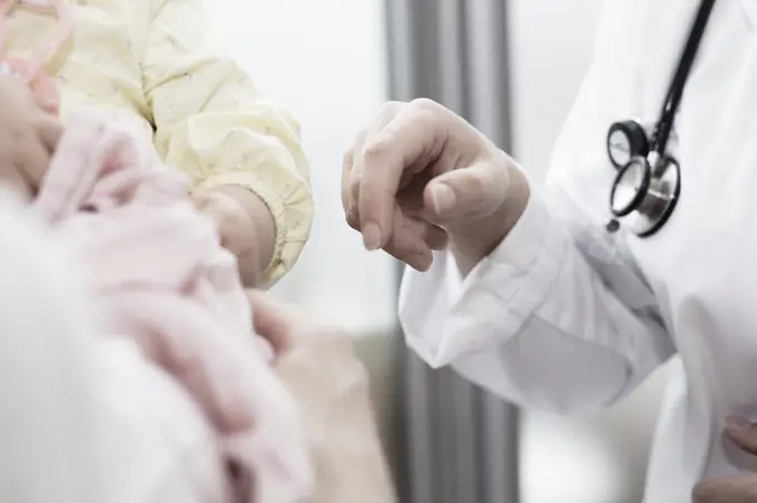 a young doctor brings her hand to a child in her mom's arms