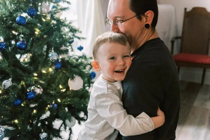 A father and son hugging and laughing by Christmas tree in living room
