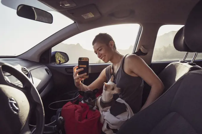 Happy person with two dogs on lap in car takes photos with phone spain