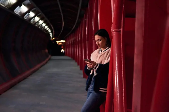 Young woman looks at her mobile phone on a red bridge. Urban scene