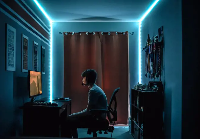 Teenage boy playing video game at desk in room with neon LED lighting.