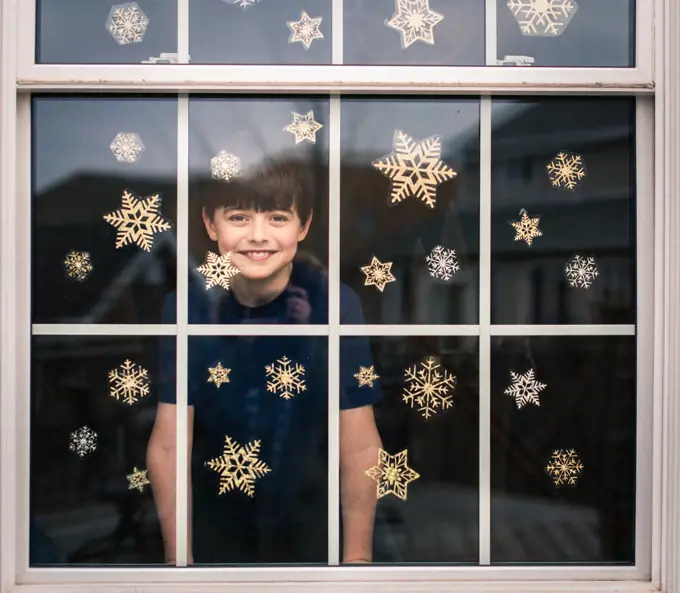 Happy boy looking out through a window covered in snowflake decals.