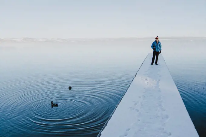 Man stands on snowy dock watching ducks swim past in Lake Tahoe