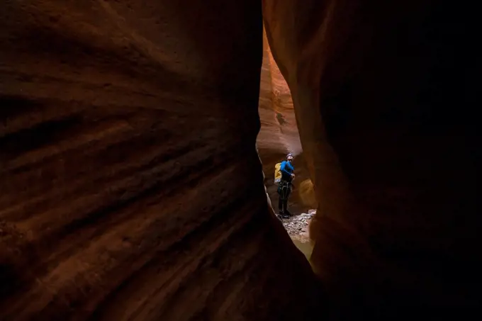 A man is seen through a small slit of red rock inside a canyon