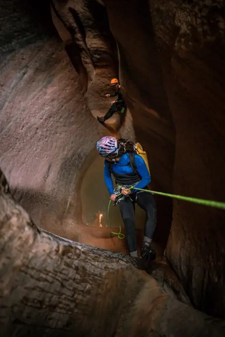 A man rappels into slot canyon while his friend waits in the distance