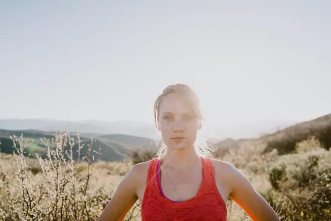 Athletic blonde woman stares back at you with sun and mountains behind