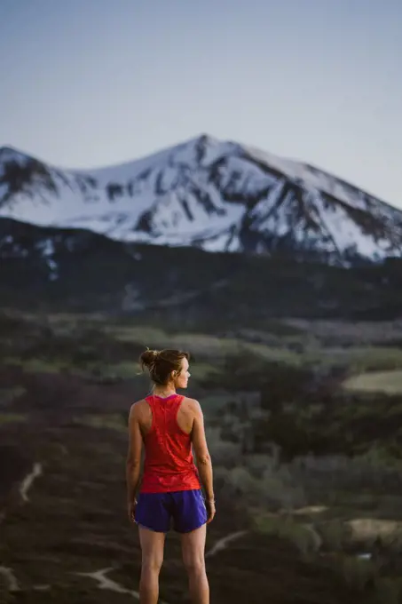 Young woman looks out at the mountains while trail running at dusk