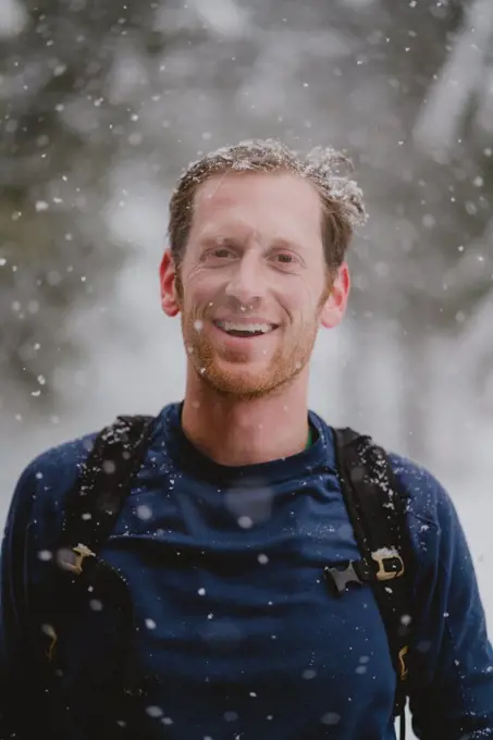 Portrait of man wearing backpack smiling with snow in hair