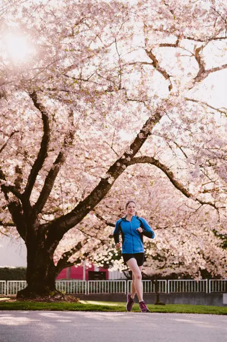 Athletic woman runs in city park in front of large cherry blossom