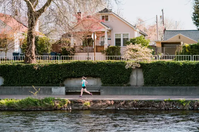 Young woman runs alongside river with houses and trees in background