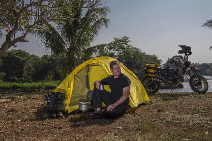 man camping next to river Kwai with his off road motorcycle