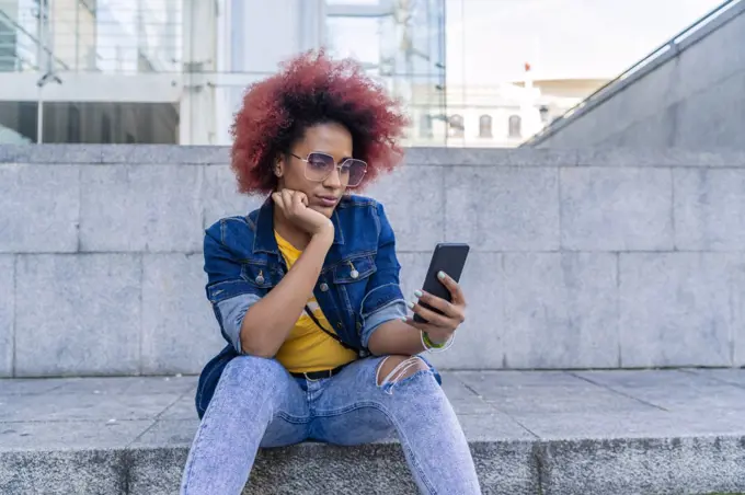 woman with afro hair with her smartphone sitting on the stairs