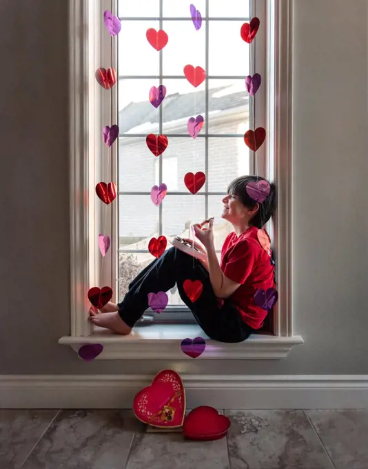 Boy eating chocolates in window decorated with hearts for Valentines.