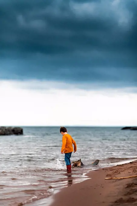 a small boy splashing his foot at the shoreline of lake superior
