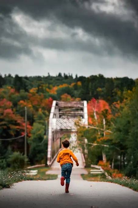 boy running towards a bridge in tree line during autumn season