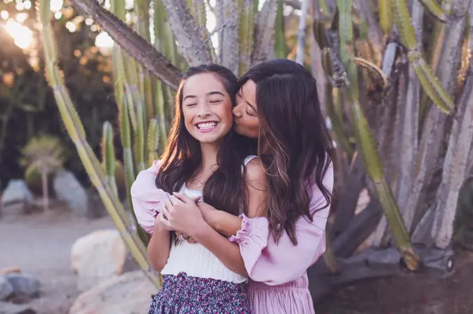 Asian mother kissing pre-teen daughter on the cheek.