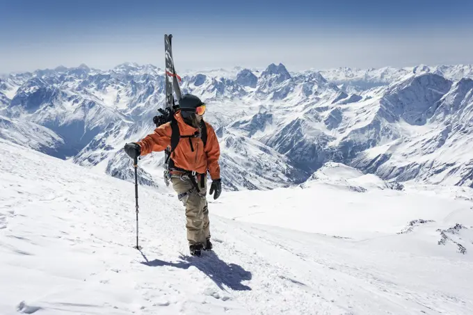 Man with ski pole carrying splitboard while climbing snowcapped mountain during vacation