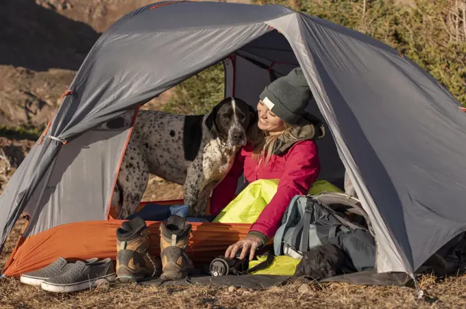 Smiling young woman with dog in tent on mountain during vacation